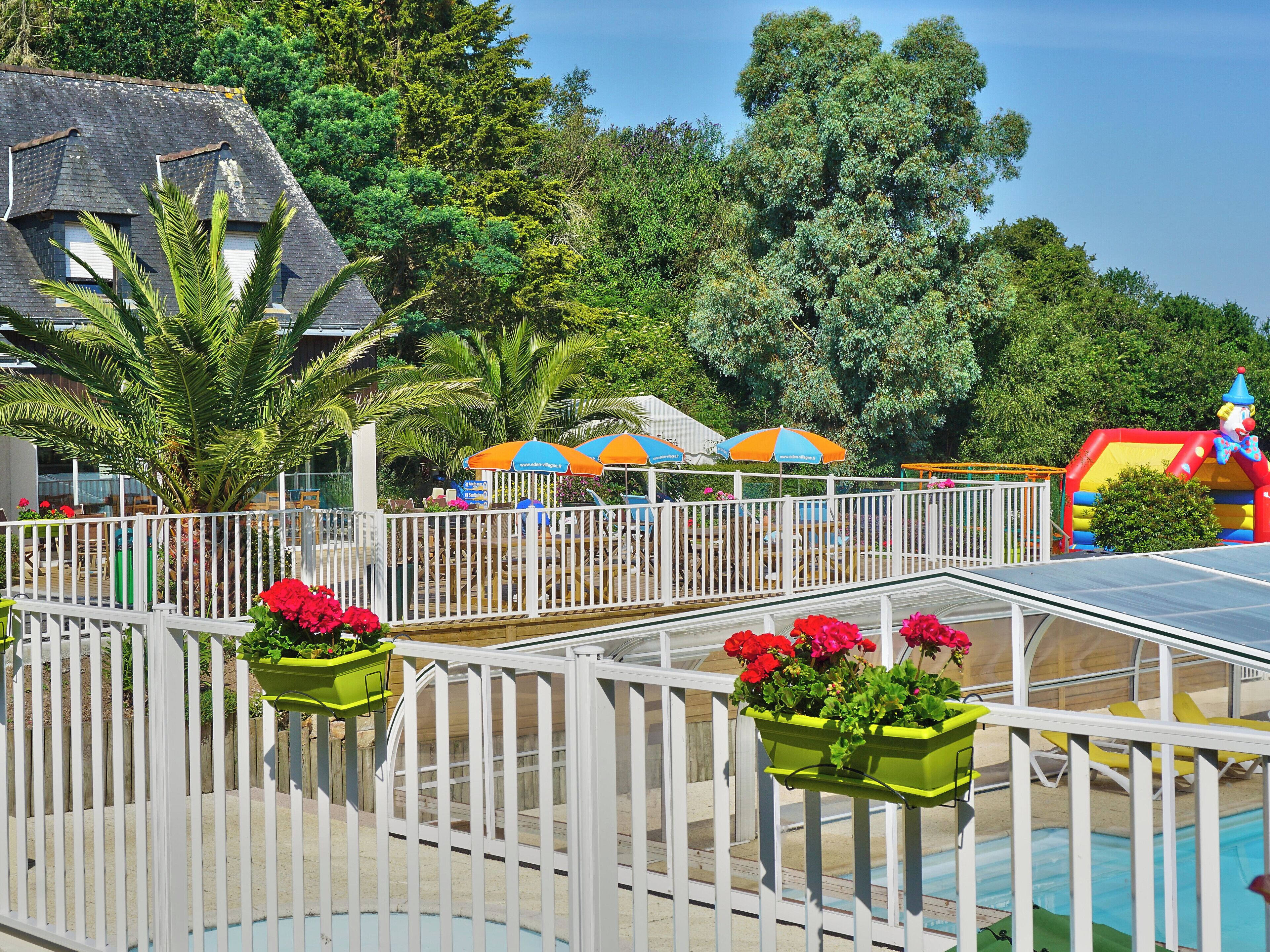 A pool area with a white fence, a slide, and colorful umbrellas.