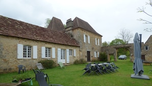 Ein Steinhaus mit Ziegeldach, Außenbereich mit Sitzgelegenheiten und ein geparktes Auto im Hintergrund.