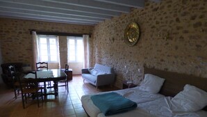 Ein Zimmer mit Steinsturz, einem Bett, einer Couch, einem Esstisch mit Stühlen und einem Fenster mit Vorhängen.