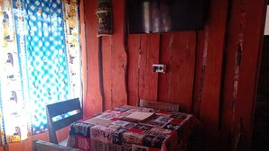 Una habitación rústica con una mesa y sillas de madera, un mantel acolchado y un televisor montado en la pared.