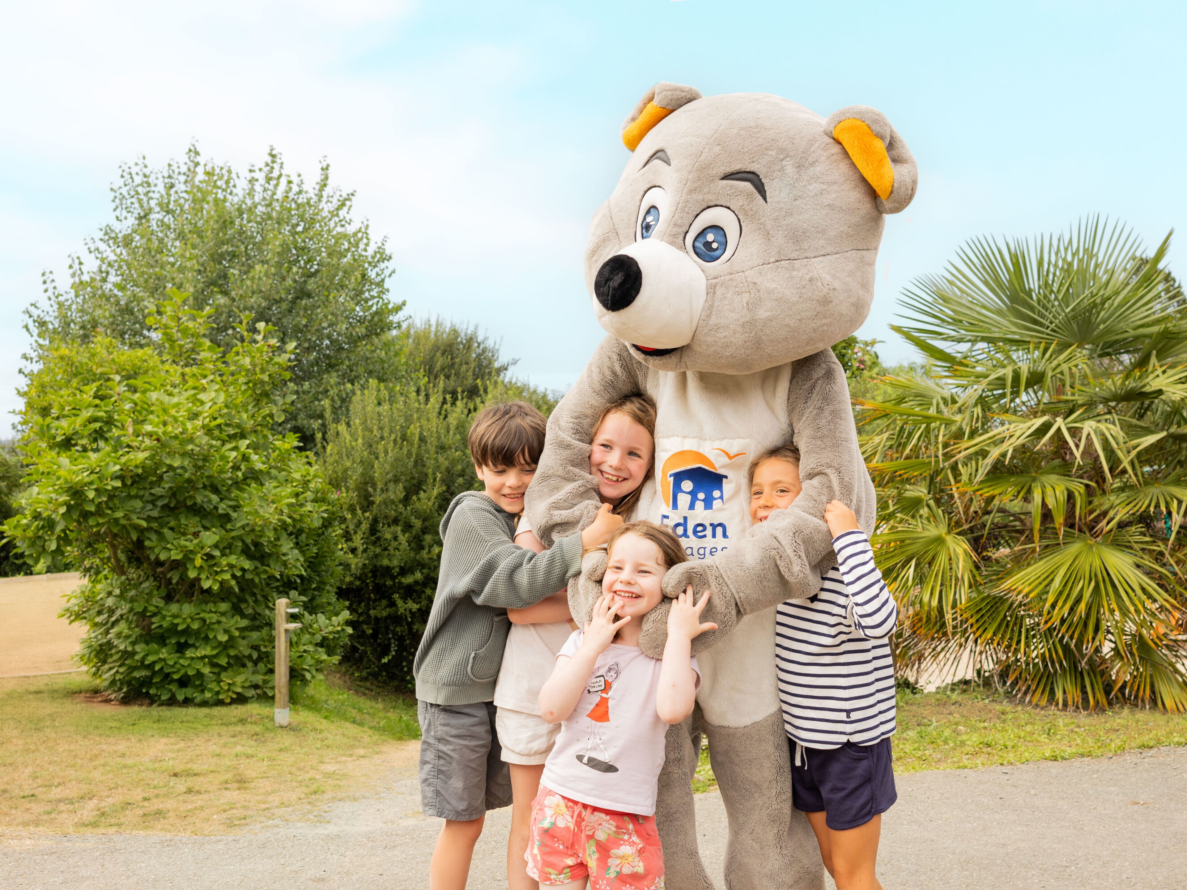Eine Gruppe Kinder umarmt eine große Teddybär-Maskotte im Freien.