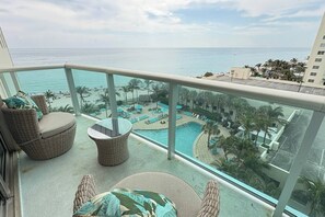 A balcony with wicker furniture, a pool area with lounge chairs, and a view of the ocean and beach. - Beachfront 2br at The Tides | Great Views (Hollywood)