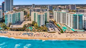 Um hotel à beira-mar com vários edifícios altos, uma praia com espreguiçadeiras e vista clara para o oceano.
