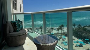 Varanda com móveis de vime, guarda-corpo de vidro e vista para a praia e o oceano.
