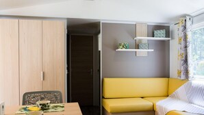 A compact room with a wooden wardrobe, a yellow sofa, a dining table with chairs, and a small shelf with decorative items. - Palmyre - Privilège 4 - 8p (Les Mathes)