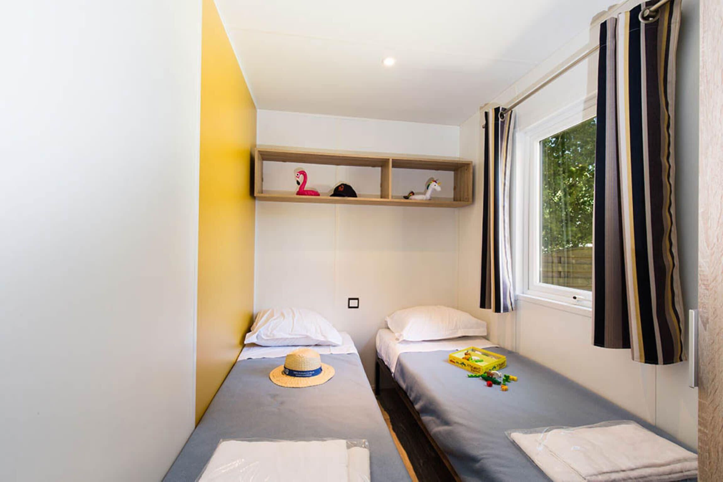 Una habitación pequeña y limpia con dos camas individuales, una estantería decorada y una ventana con cortinas.