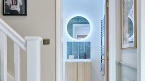Ein Flur, der zu einem Badezimmer mit einem runden Spiegel, einem Waschbecken und einem Handtuchhalter führt.