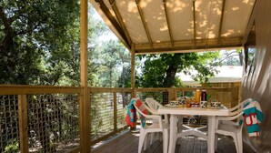 Eine überdachte Terrasse im Freien mit Tisch und Stühlen, umgeben von einem Holzzaun und Bäumen.