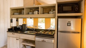 Cocina compacta con estufa a gas, microondas, refrigerador y estantes de madera sobre la encimera.