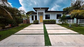 Una casa moderna de dos pisos con una puerta amarilla, cerca viva blanca y un césped bien cuidado.