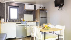 Una cocina moderna con lavavajillas integrado, estufa y refrigerador. Hay una mesa de comedor con sillas blancas y un televisor montado en la pared.
