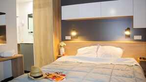 Una habitación de hotel con una cama, una mesita de noche, un armario de madera y un espejo.