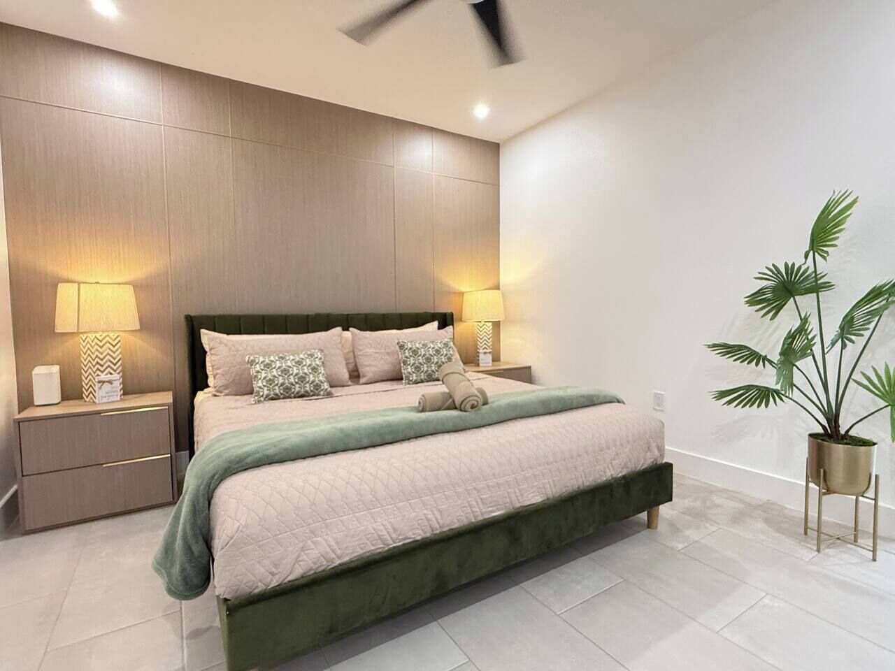 Quarto moderno com uma cama grande, abajures, ventilador de teto e um vaso de planta.