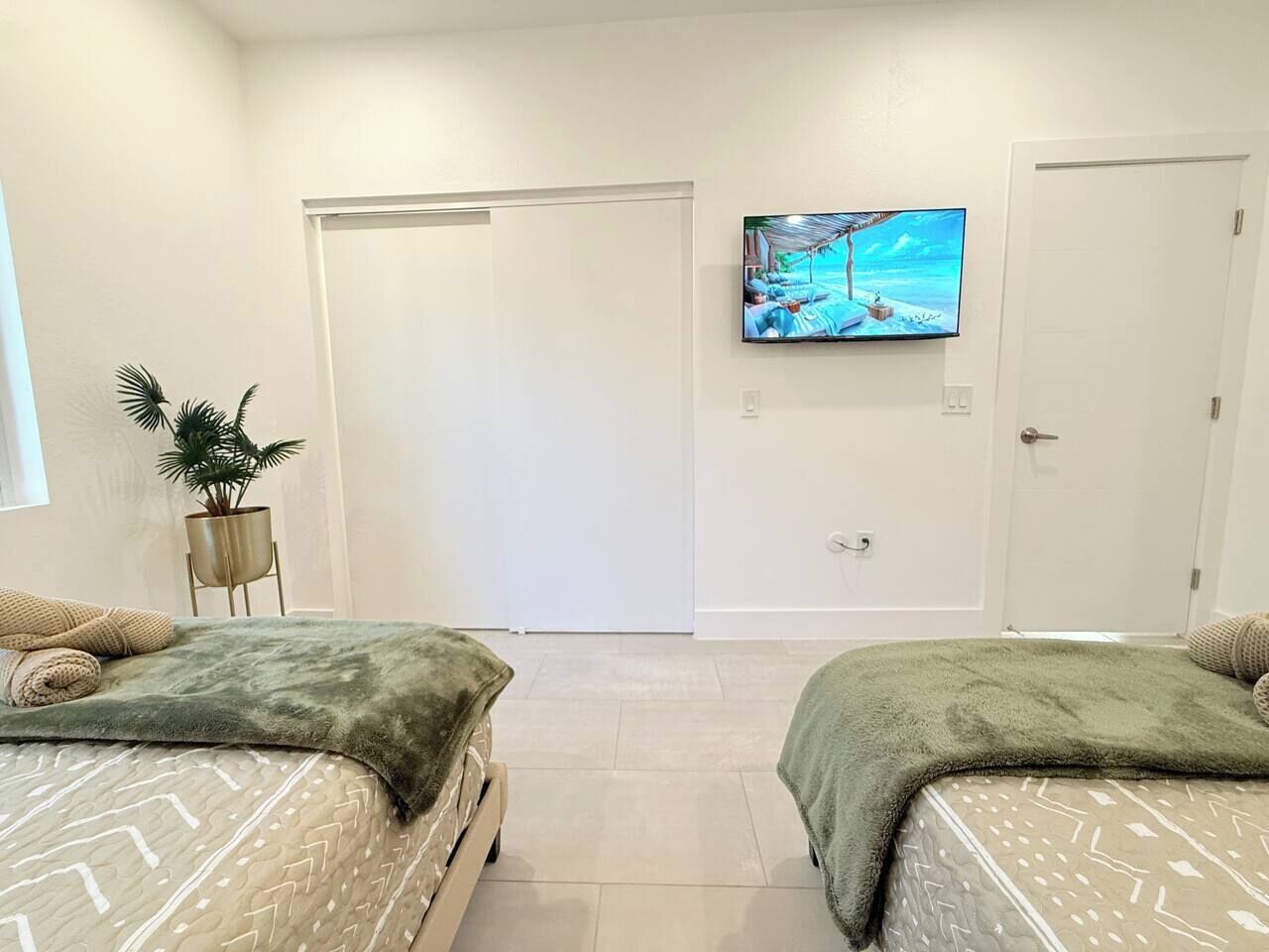 A hotel room with two beds, a TV on the wall, and a potted plant.