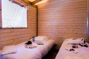 A wooden cabin room with two beds, a window, and various personal items on the beds. - Palmyre - Eco-lodge 2 - 4p (2) (Les Mathes)