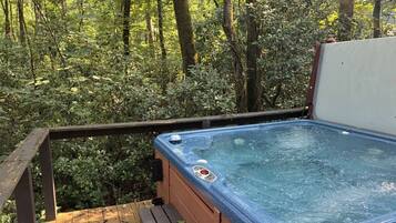 A hot tub on a wooden deck surrounded by dense forest.