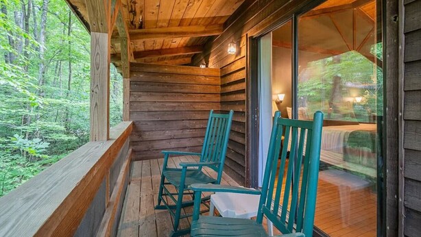 Una cabaña de madera con un porche que tiene dos sillas verdes y una mesa.
