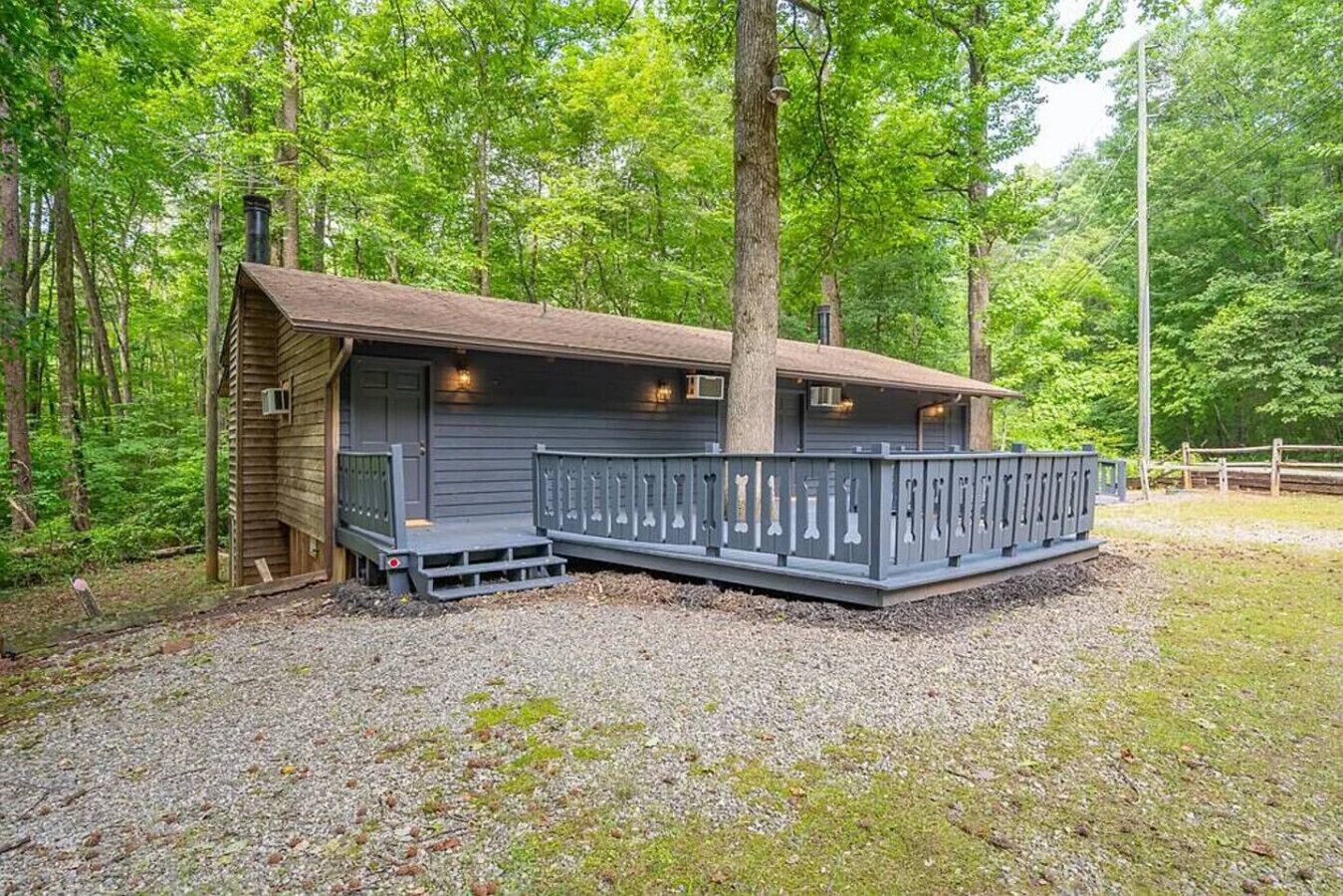 Une cabane dotée d’une terrasse et d’une cheminée, entourée d’arbres.
