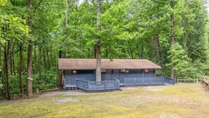 A cabin with a porch and a fenced yard, surrounded by trees.