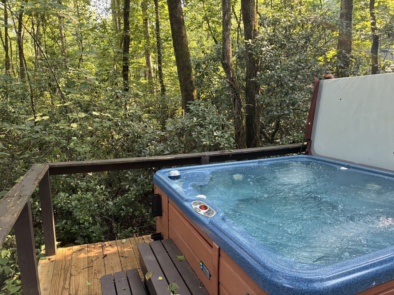 Een hottub op een houten terras, omgeven door dicht bos.