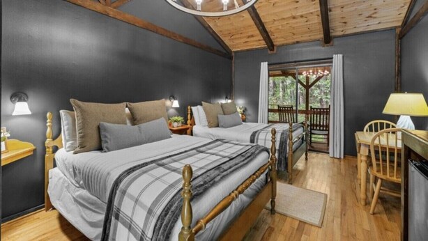 Une chambre avec deux lits, des poutres en bois, un lustre et une vue sur l’extérieur, visible à travers une porte.