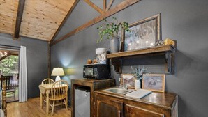 A compact kitchen with a wooden cabinet, a sink, and a microwave. There is a small dining area with a chair and a table. - The Lost Compass - Suite #2 - Cozy Cabin Retreat (Sautee Nacoochee)