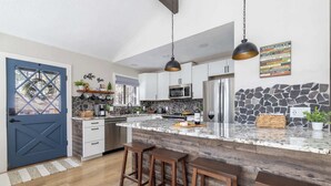 A modern kitchen with a stone backsplash, stainless steel appliances, and a bar area with stools. - Modern Cabin Retreat w/ Deck & BBQ (Flagstaff)