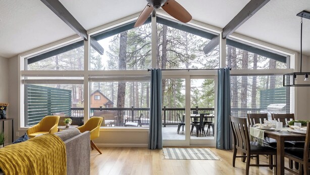 A spacious room with a high ceiling, large windows, and a view of a forested area. - Modern Cabin Retreat w/ Deck & BBQ (Flagstaff)