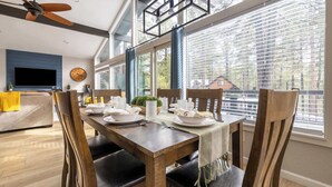 A dining area with a wooden table set for four, surrounded by chairs with leather cushions. A ceiling fan is visible above, and there is a large window with blinds to the right. - Modern Cabin Retreat w/ Deck & BBQ (Flagstaff)