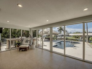 A spacious room with large windows, a pool, and a chair with a starfish pillow. - Casa Tiki - Pool, Canal, Dock, Tiki Hut, Bar & BBQ (Cape Coral)