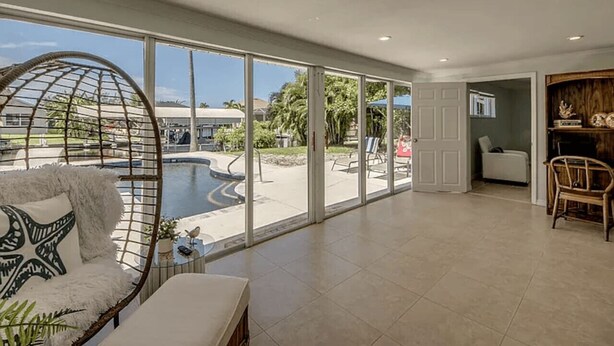 Amplia sala de estar con ventanas grandes, piscina y una silla colgante.