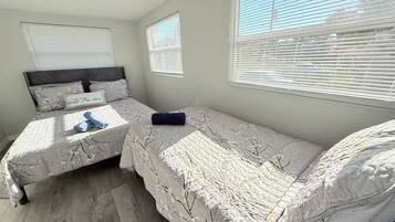 Een slaapkamer met twee bedden, een groot raam met zonwering en uitzicht op de omgeving.