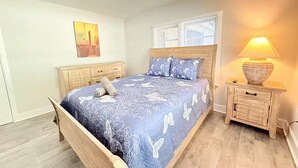 Ein Schlafzimmer mit einem Holzbett, einem Nachttisch mit Lampe, einem Fenster mit Jalousien und einem Gemälde an der Wand.