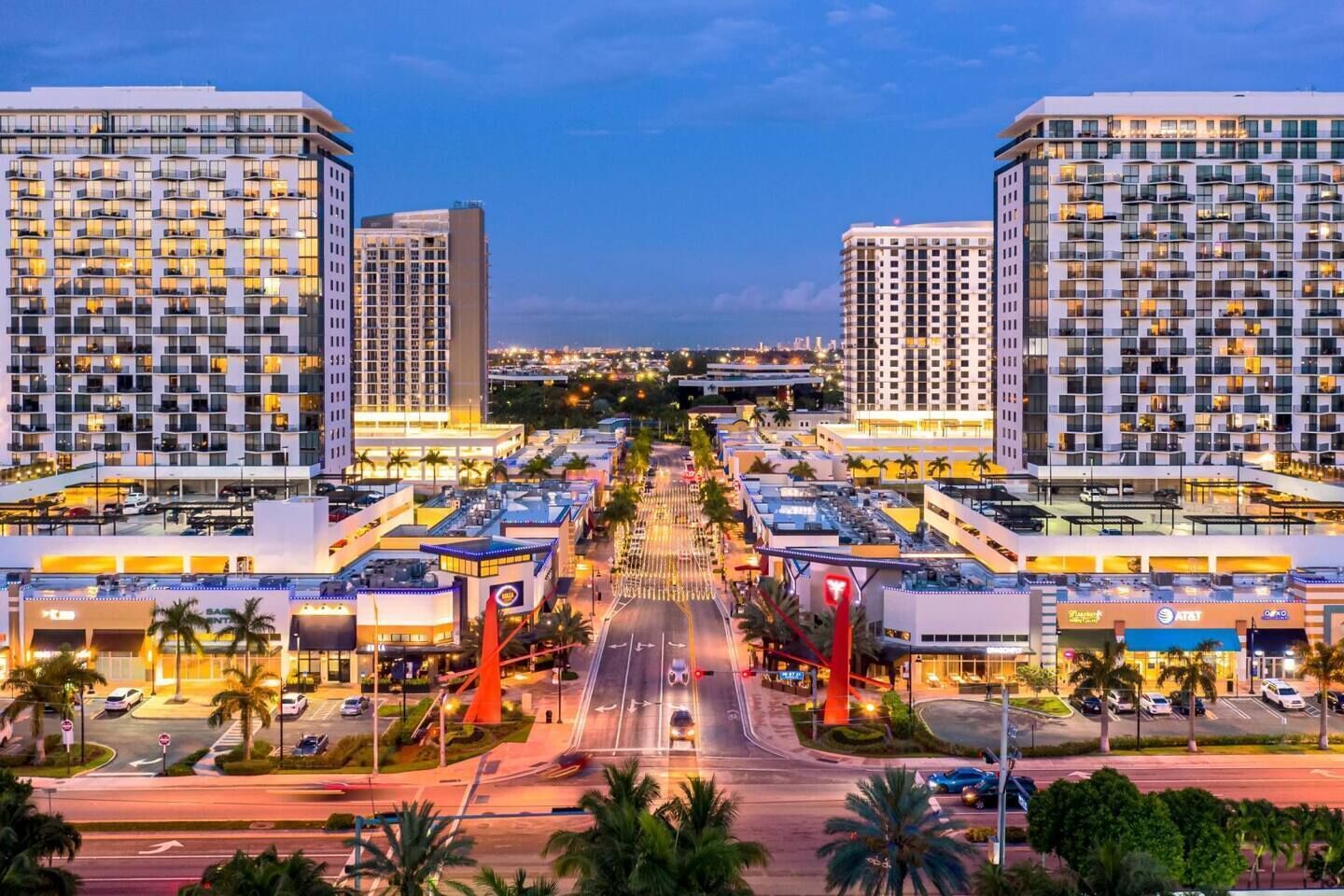 Un moderno complejo hotelero con varias torres altas, una avenida central y palmeras que lo rodean.