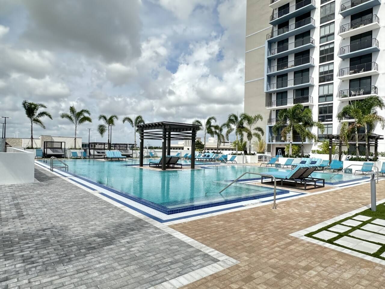 A hotel pool area with a gazebo, lounge chairs, and palm trees.