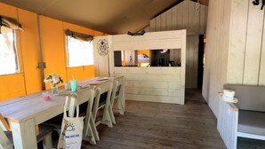 A cozy room with a wooden dining table, chairs, and a bench. A small kitchen area is visible in the background. - Palmyre - Eco-lodge 3 - 7p (1) (Les Mathes)