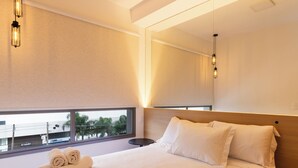 A hotel room with a large bed, a bedside table, and a window with a view of a building and trees. - Edifício Nex One by Wecare Hosting (São Paulo)