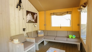 A cozy room with a wooden floor, a sofa, a chair, a small table with a hat and a magazine, and a window with a curtain. - Palmyre - Eco-lodge 3 - 7p (6) (Les Mathes)