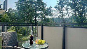 Een balkon met een rieten stoel, een tafel met een fles wijn, glazen en een schaal druiven.