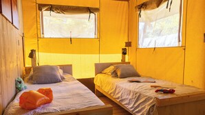 A room with two wooden beds, each with a headboard, a window with a curtain, and a small table with a book and a toy. - Palmyre - Eco-lodge 3 - 7p (10) (Les Mathes)