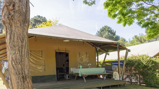 Alojamiento rústico al aire libre con una zona de estar cubierta, una mesa y un banco.