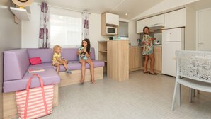 A modern living room with a purple sofa, a kitchen area, and a dining table with a white chair. - Palmyre - Confort 2 - 5p (5) (Les Mathes)