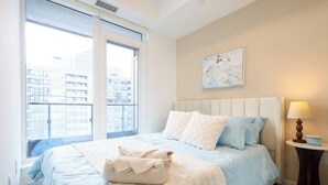 A bedroom with a bed, a window, a painting, and a bedside table with a lamp. - The Calm House | 5 mins Walk to Square One Mall (Mississauga)