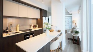 A modern kitchen with dark cabinetry, a white countertop, and a central island. There is a dining area with a table and chairs visible in the background. - The Calm House | 5 mins Walk to Square One Mall (Mississauga)