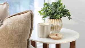 A beige sofa with a cushion, a small round table with a plant and two containers, and a window with a view of buildings. - The Calm House | 5 mins Walk to Square One Mall (Mississauga)