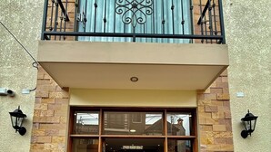 A building entrance with a glass door, a balcony with a metal railing, and stone-patterned walls. - Peaceful Apartment in Sucre, steps from the Downtown (Sucre)