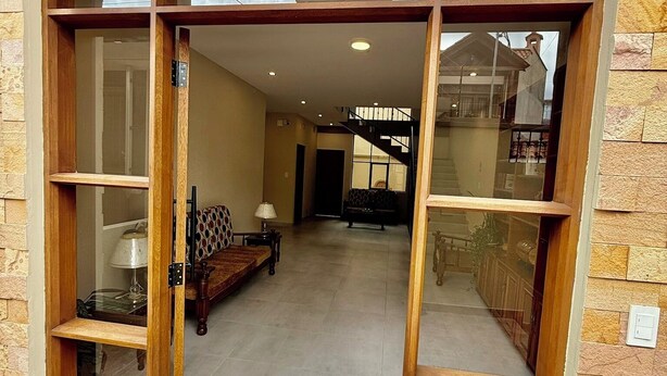 A spacious entrance with a wooden frame and glass doors, leading into a well-lit interior with a staircase and a sofa. - Peaceful Apartment in Sucre, steps from the Downtown (Sucre)
