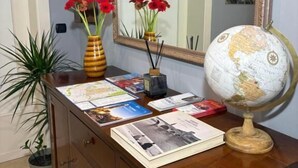 Un aparador de madera con un globo terráqueo, un espejo y un florero con flores rojas.