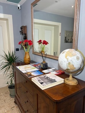 Une commode en bois, sur laquelle on trouve un globe terrestre, un miroir et un vase rempli de fleurs rouges.
