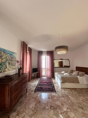 Een slaapkamer met een bed, een kaptafel, een schilderij, een spiegel en een raam met gordijnen.
